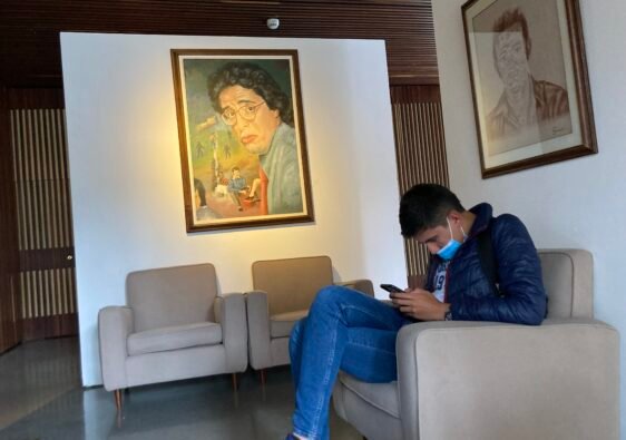 Exposición de Jaime Garzón en El Centro de Memoria de Bogotá. Se ve un joven sentado escuchando un video que se presenta en la exposición, al fondo se ve una obra con la cara de Garzón
