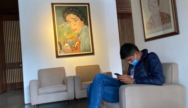 Exposición de Jaime Garzón en El Centro de Memoria de Bogotá. Se ve un joven sentado escuchando un video que se presenta en la exposición, al fondo se ve una obra con la cara de Garzón