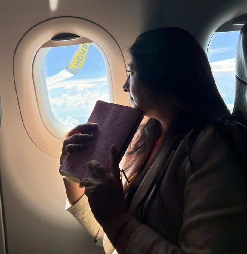 Diana en la ventana de un avión con un libro en la mano