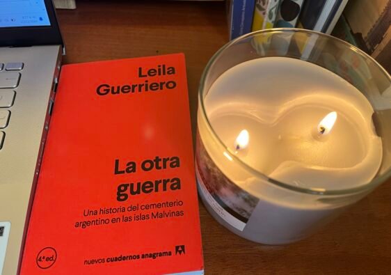 Portada del libro La otra Guerra de Leila Guerriero junto al computador y una vela encendida