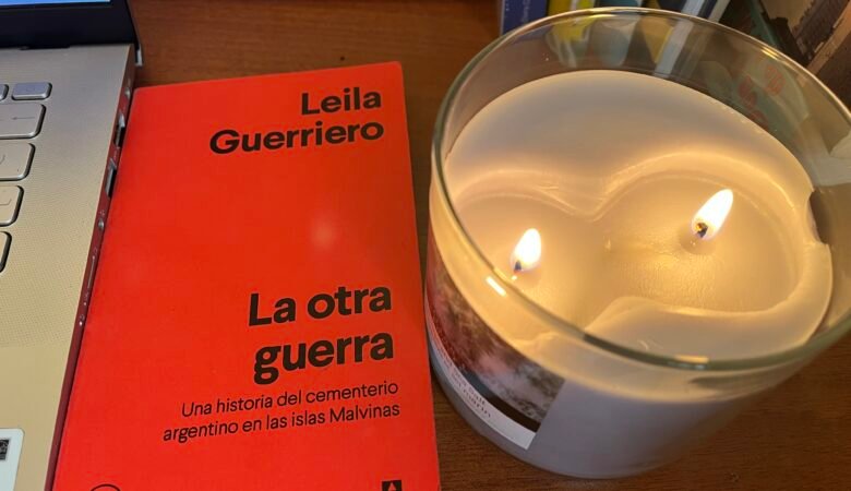 Portada del libro La otra Guerra de Leila Guerriero junto al computador y una vela encendida