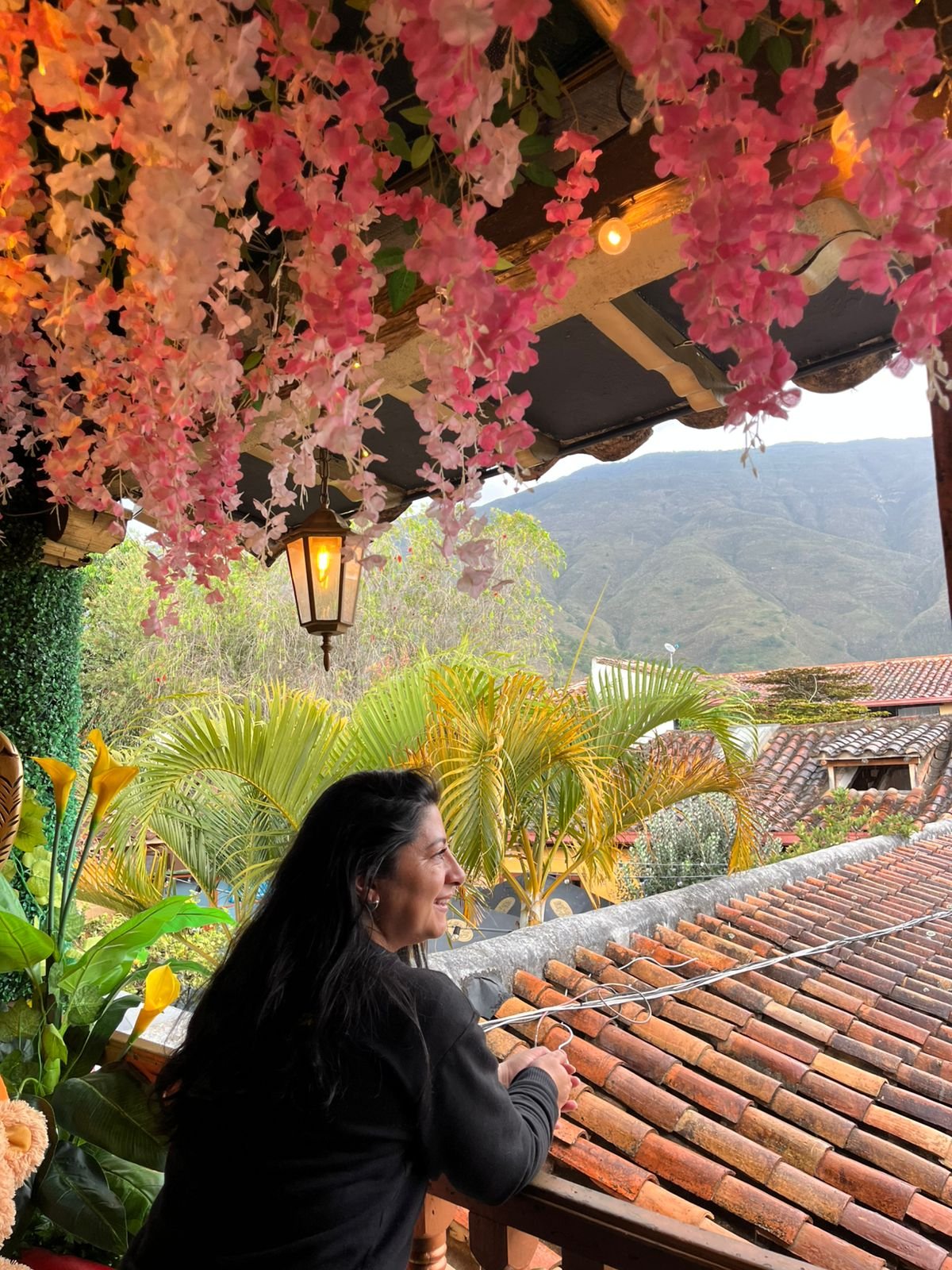 Villa de Leyva Boyacá Colombia. Balcón del Museo de Chocolate. Foto: Nury Socha. Se ve un farol sobre la cabeza de Diana, quien mira el tejado de los locales vecinos, la montaña y la lluvia caer.