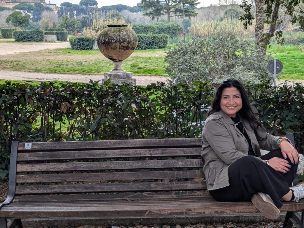 Diana sentada en la banca de Villa Borghese, detrás unos arbustos y una de las plazas.