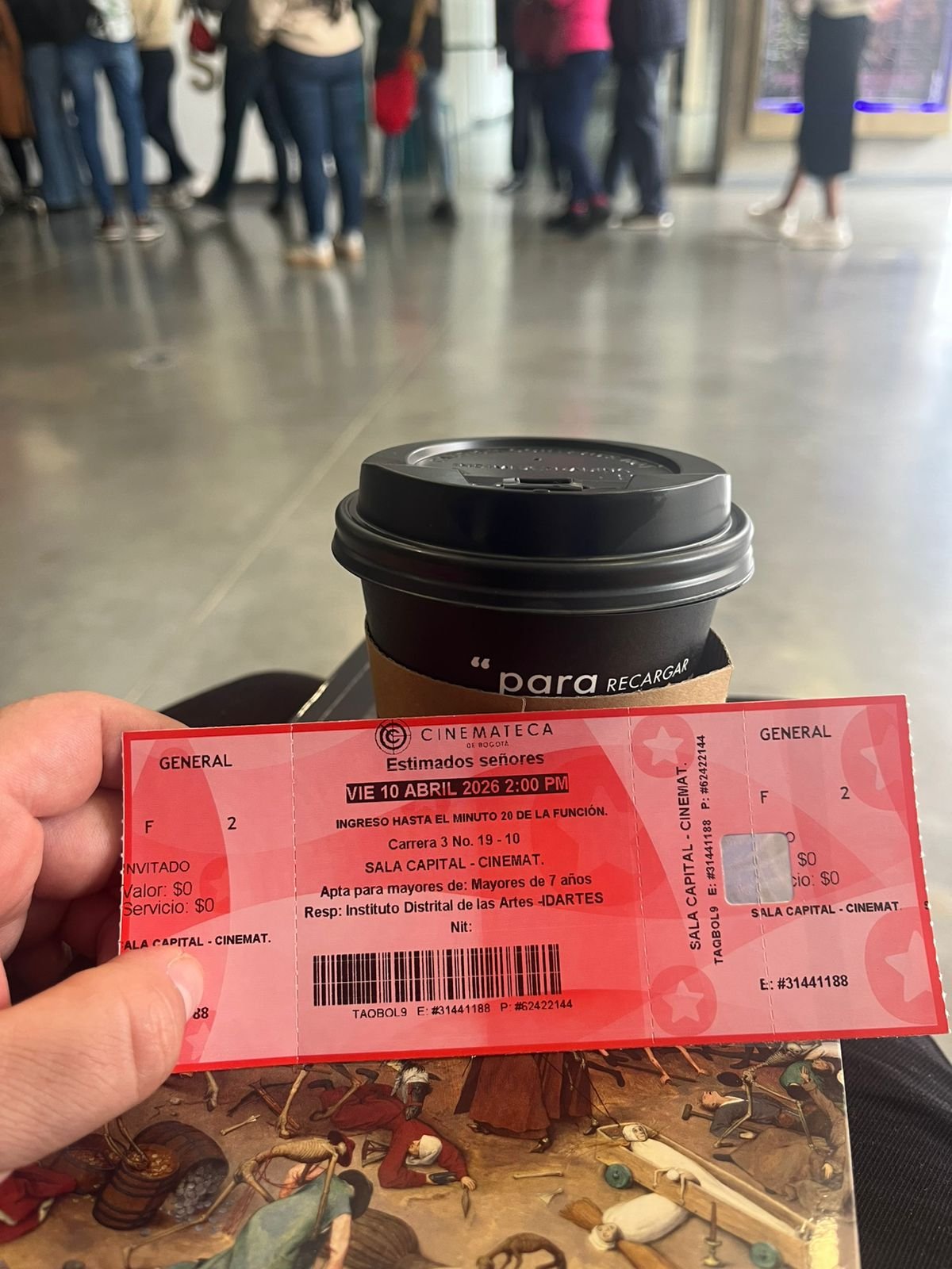 Tiquete de entrada a la película Estimados Señores, junto a un café y al frente la fila de ingreso
