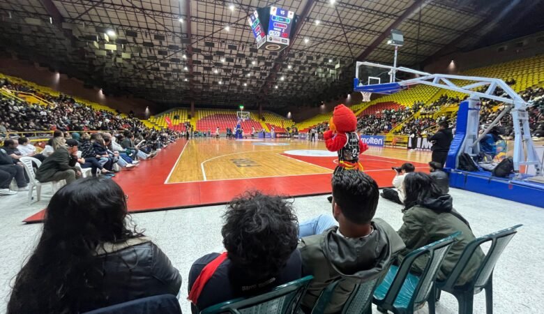 Cuatro sillas instaladas frente a la cancha. Cuatro personas y la mascota de Piratas viendo de cerca el partido de baloncesto
