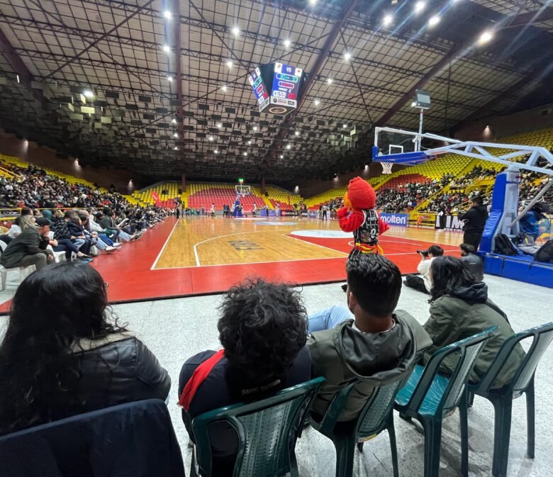 Cuatro sillas instaladas frente a la cancha. Cuatro personas y la mascota de Piratas viendo de cerca el partido de baloncesto
