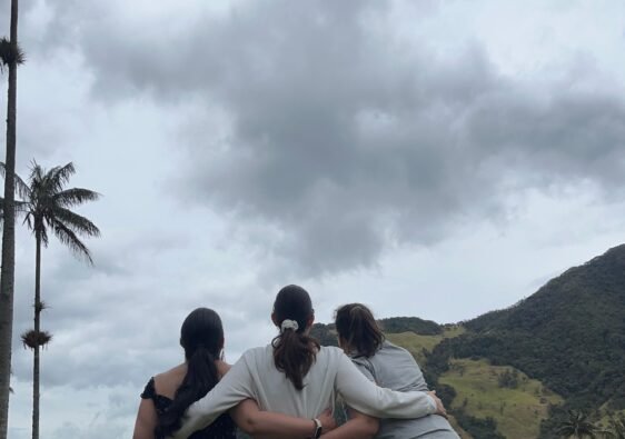Tres amigas abrazadas mirando el paisaje del Valle del Cocora. Montañas, cielo nublado y las palmeras gigantes