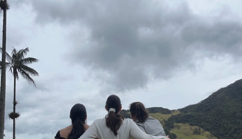 Tres amigas abrazadas mirando el paisaje del Valle del Cocora. Montañas, cielo nublado y las palmeras gigantes