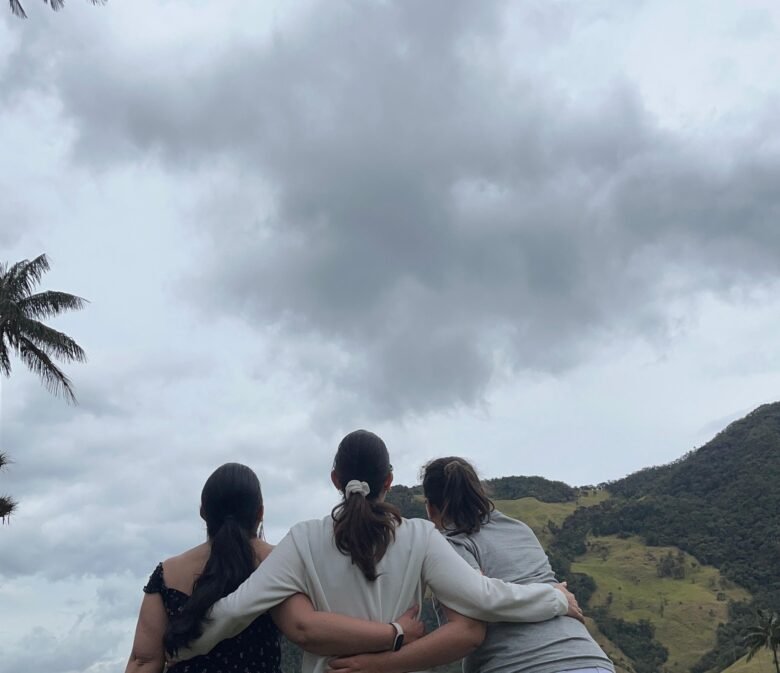 Tres amigas abrazadas mirando el paisaje del Valle del Cocora. Montañas, cielo nublado y las palmeras gigantes