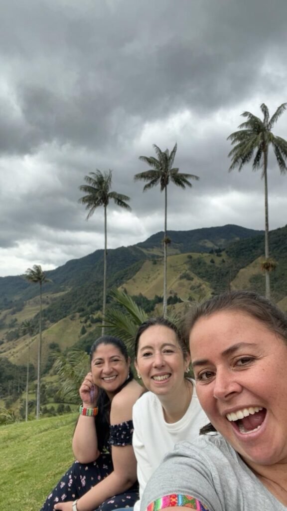 Al fondo el cielo gris, con nubes, tres palmeras gigantes una montaña y tres amigas: Diana, Maritza y Carmen en el Valle del Cocora
