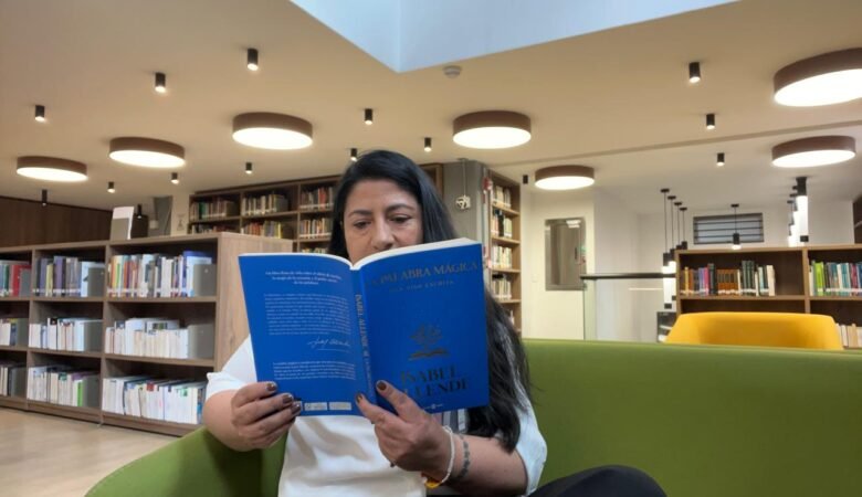 Diana en una biblioteca, al fondo se ven libros y ella está sentada en un sofá verde leyendo la palabra mágica de Isabel Allende