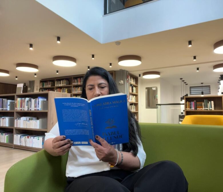 Diana en una biblioteca, al fondo se ven libros y ella está sentada en un sofá verde leyendo la palabra mágica de Isabel Allende