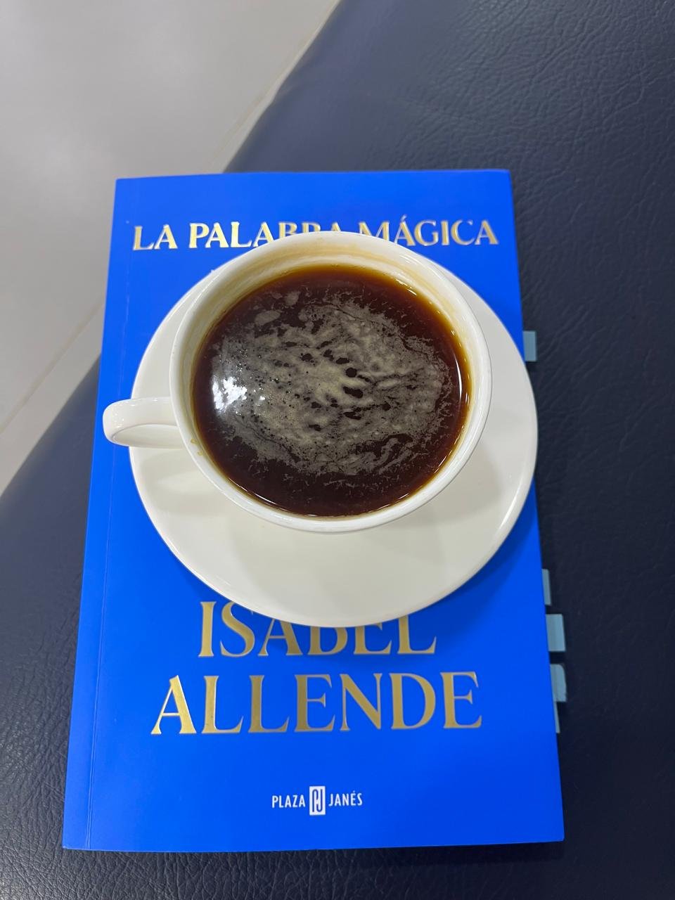 Una mesa, el libro la palabra mágica de Isabel Allende y encima una taza de café.