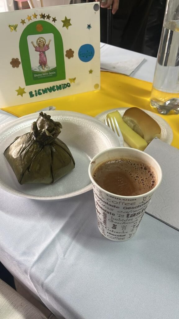 Chocolate, tamal, queso y pan sobre la mesa y un aviso con la bienvenida y el logo de las damas salesianas